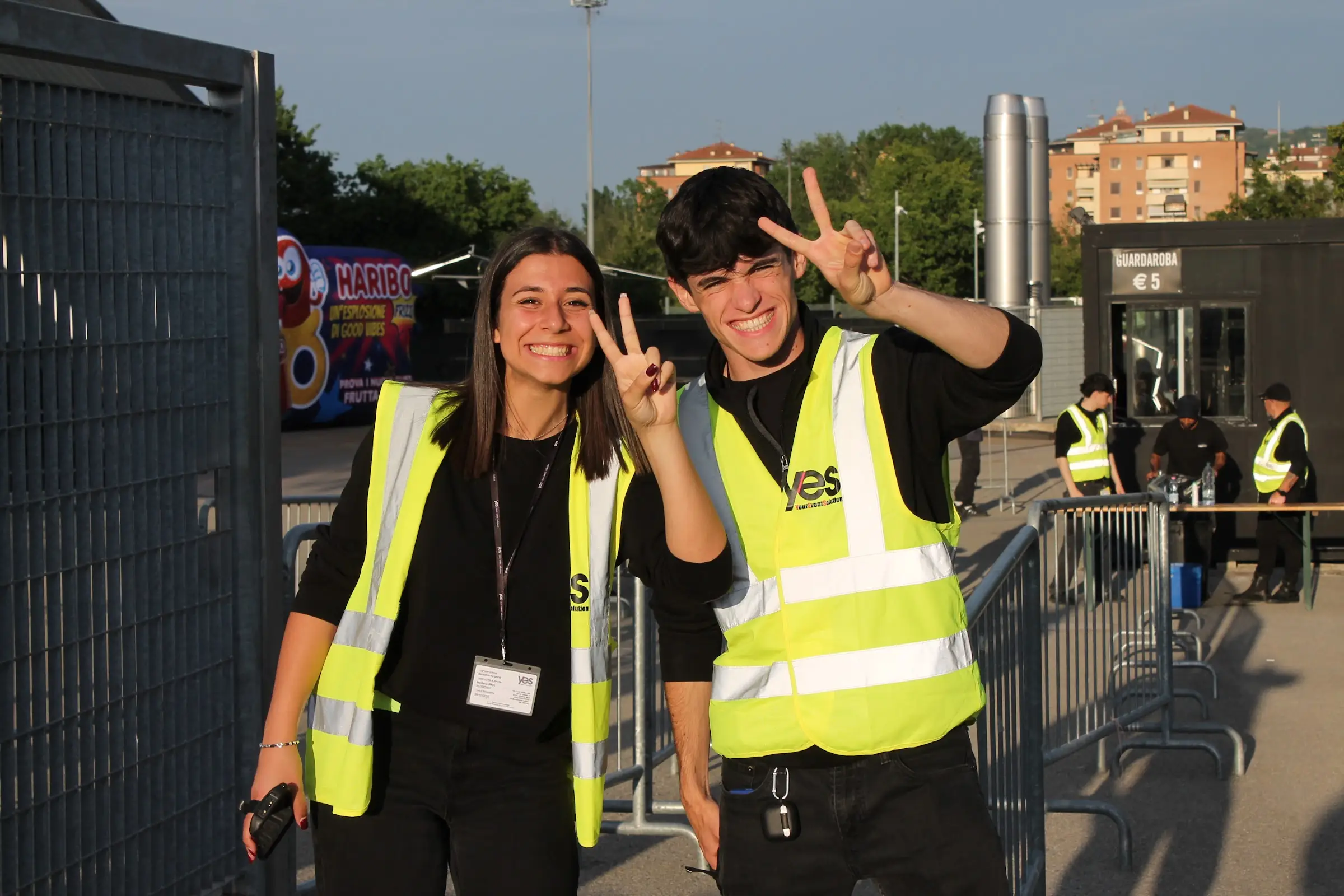 Due giovani operatori YES in pettorina sorridono e fanno il segno della pace all'ingresso di un evento