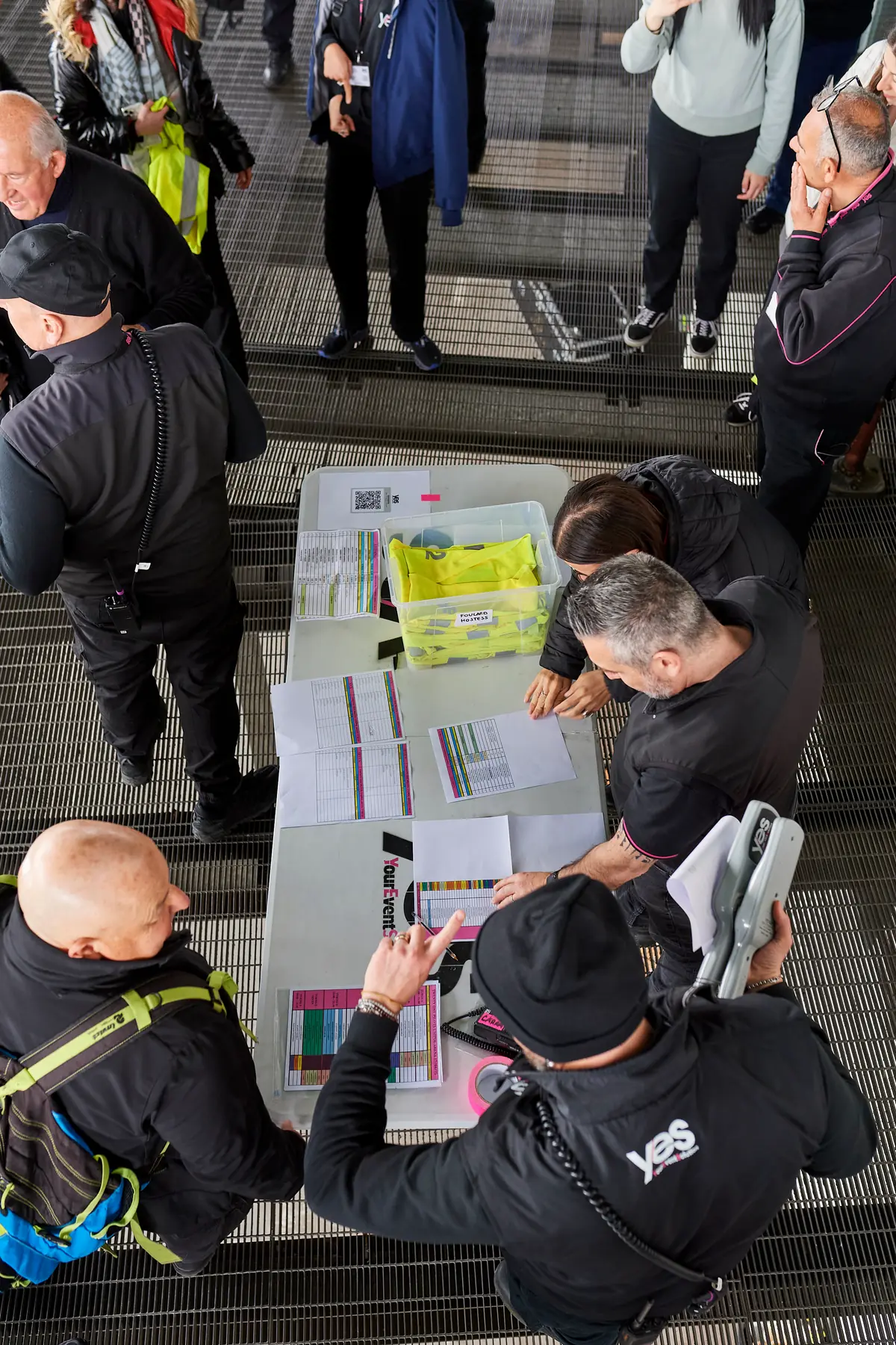 Dall'alto, il tavolo dell'accredito YES: i coordinatori consegnano pettorine, radio e fogli di servizio agli operatori prima di un evento