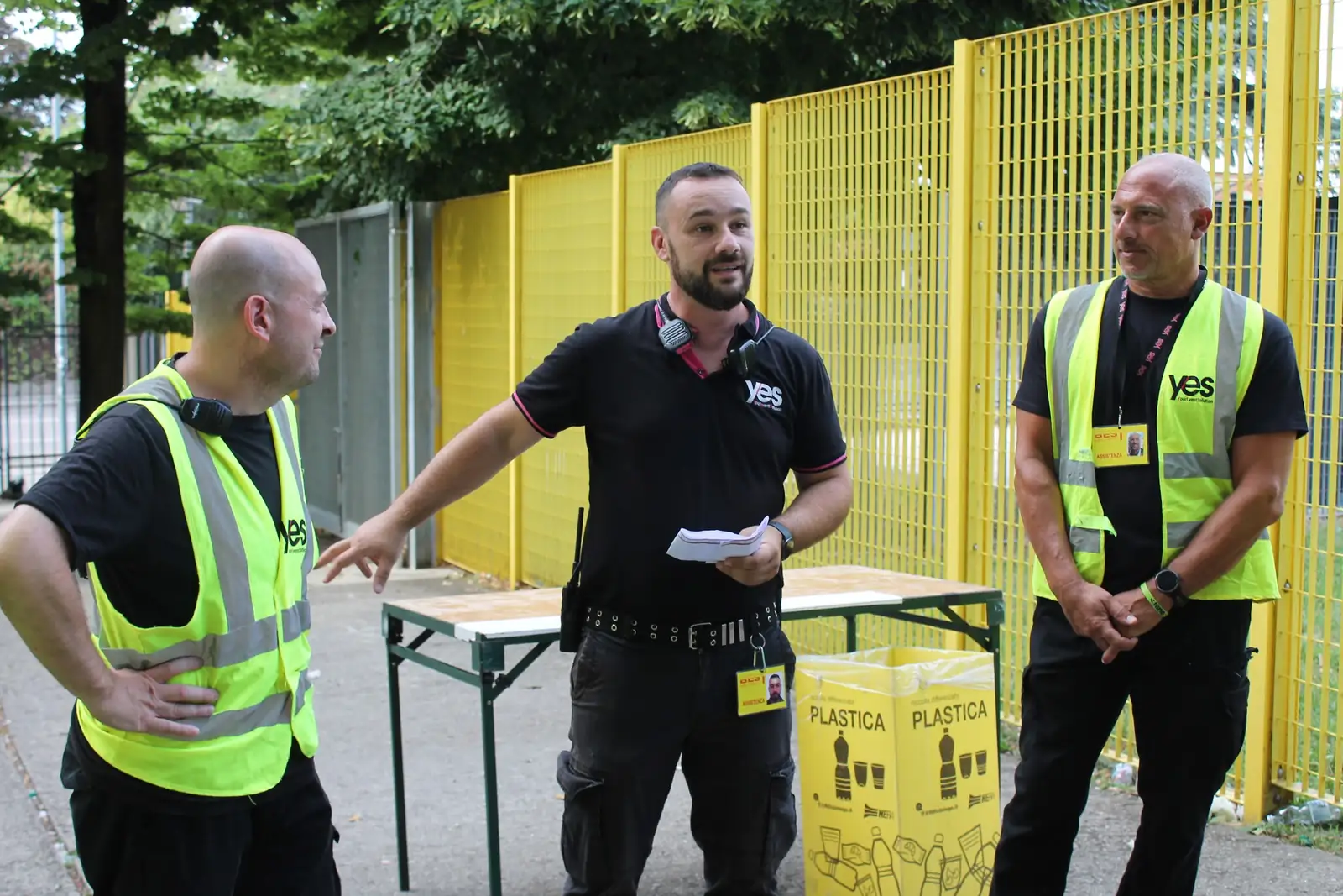 Un coordinatore YES spiega le postazioni del piano di sicurezza a due steward in pettorina gialla, prima dell'apertura