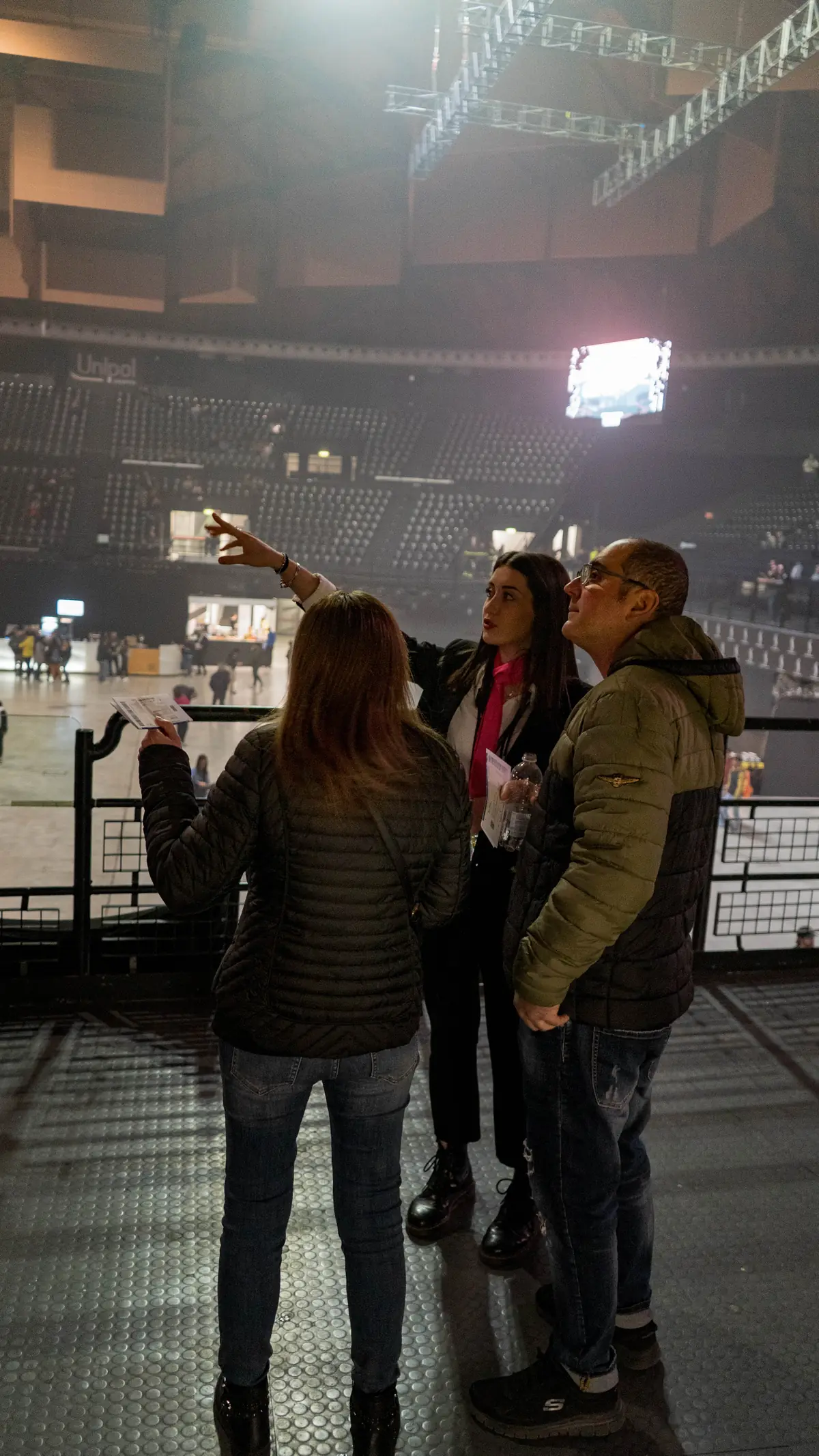 Una hostess YES con il foulard fucsia indica il posto a due spettatori sulle tribune dell'Unipol Arena