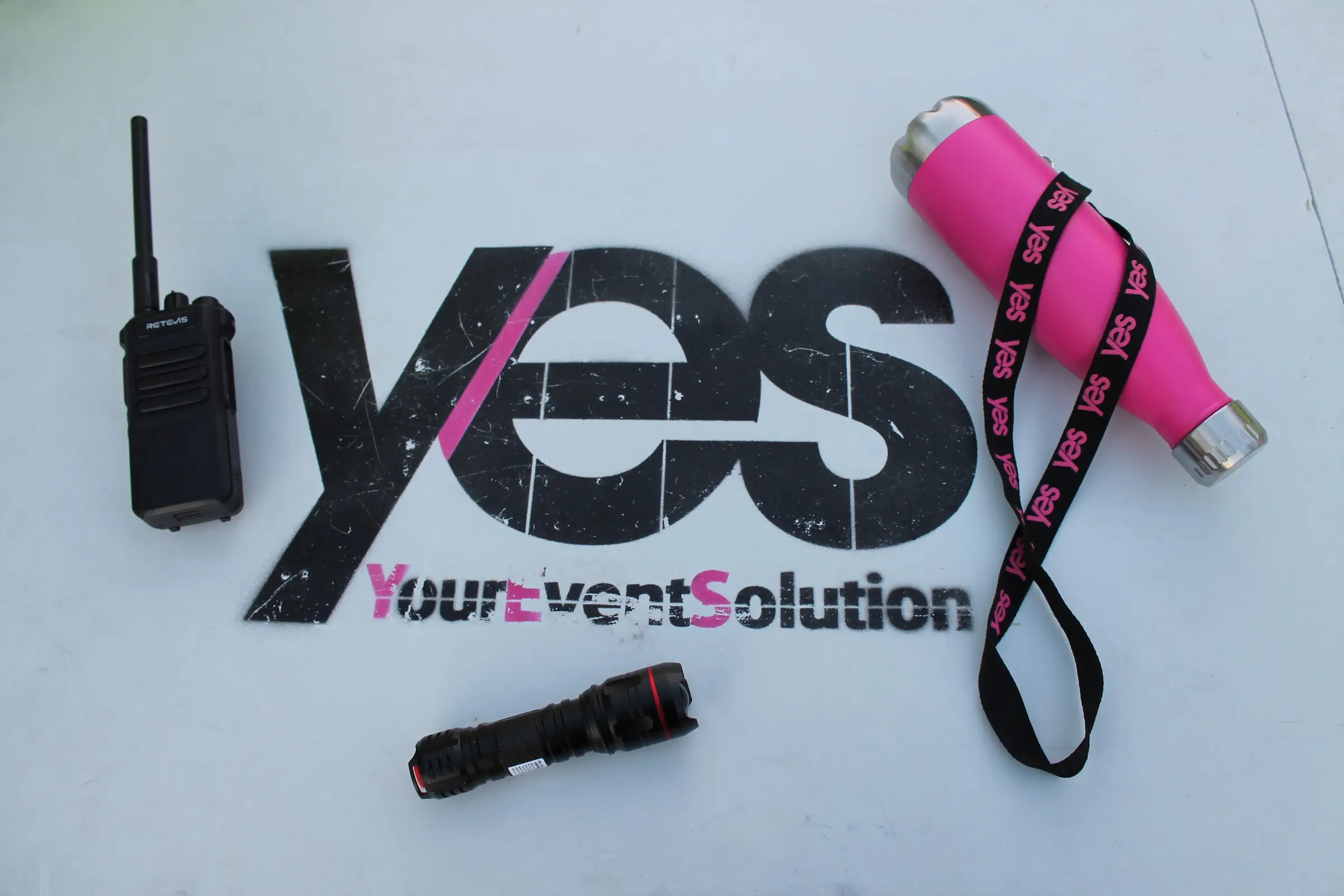 Il logo YES dipinto su un tavolo, con la radio, la torcia e la borraccia rosa con il laccetto YES di un operatore
