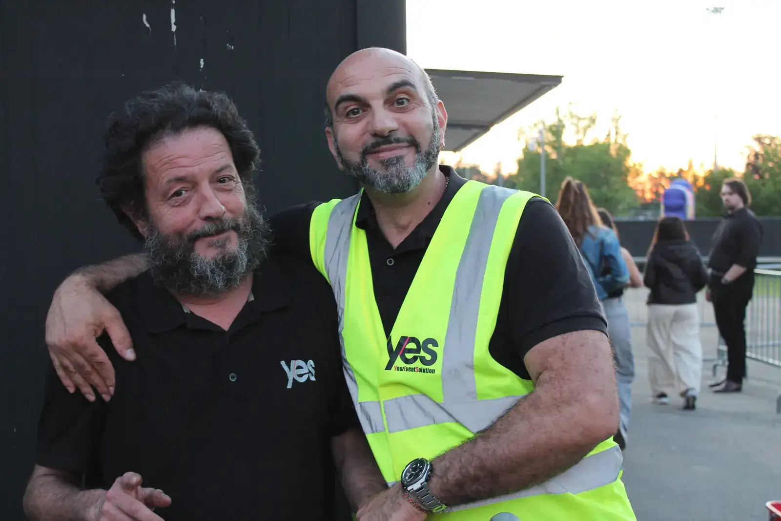 Due operatori YES sorridono abbracciati prima dell'apertura dei cancelli, al tramonto