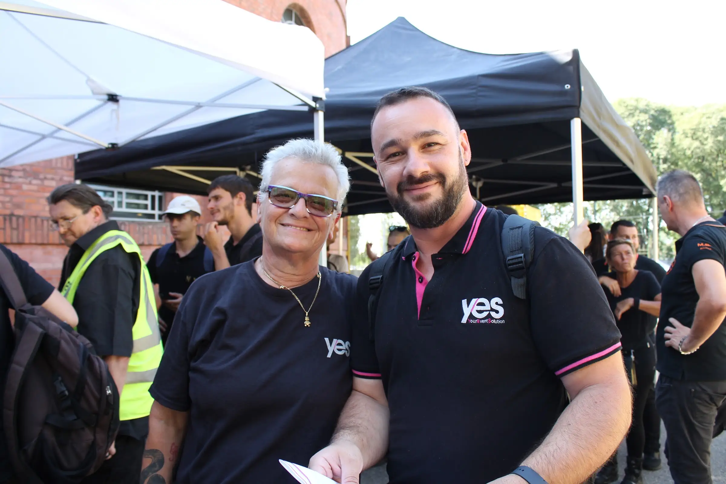 Due referenti YES con la polo aziendale sorridono sotto i gazebo del backstage, prima di un evento