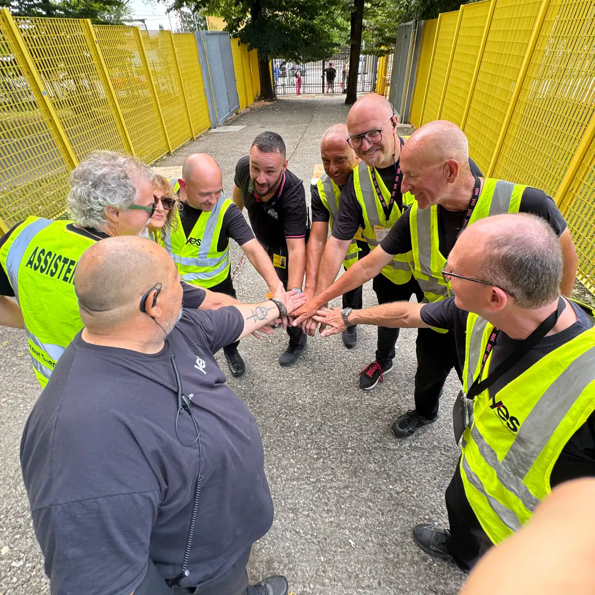 Gli steward YES in pettorina gialla uniscono le mani in cerchio prima dell'inizio di un evento